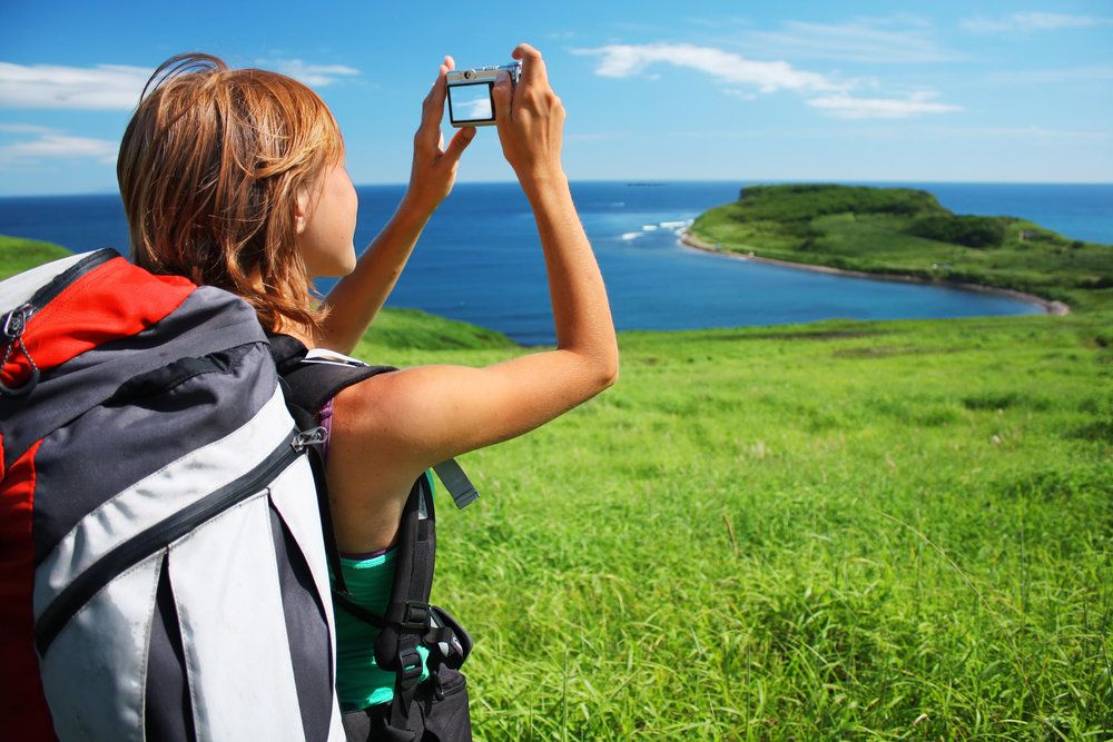 View from behind of woman backpacking, taking photo of ocean from overlook